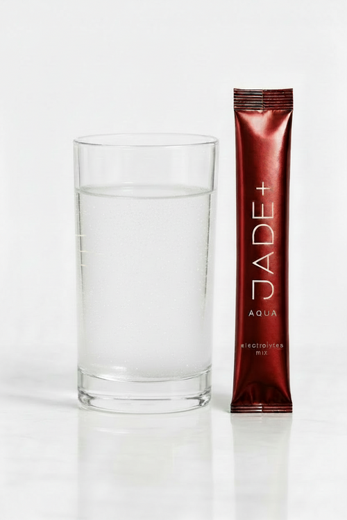 Red JADE+ electrolytes mix packet next to a glass of water on a white background